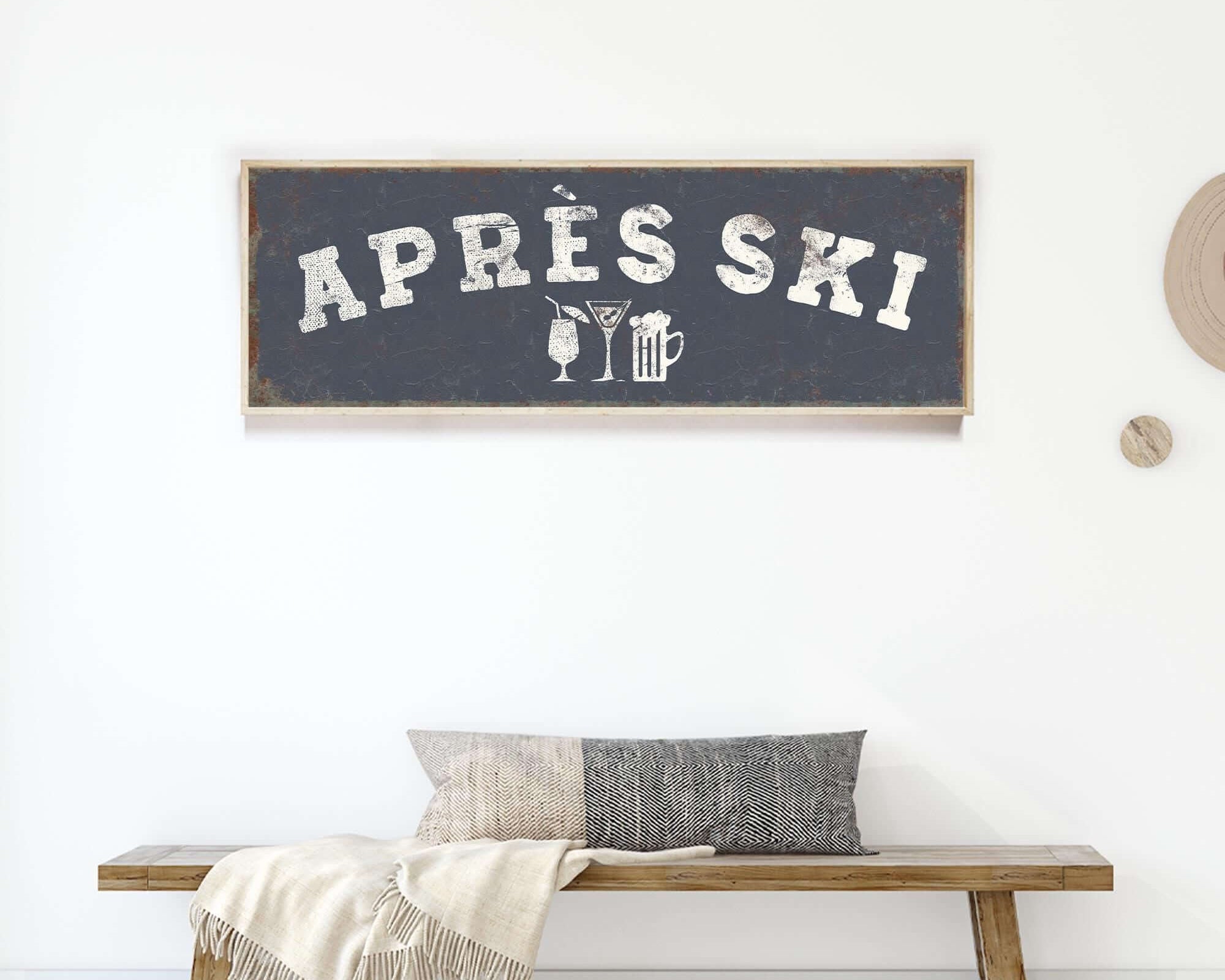 a wooden bench with a gray and white throw blanket on it, and a framed sign above it that says "APRES SKI".