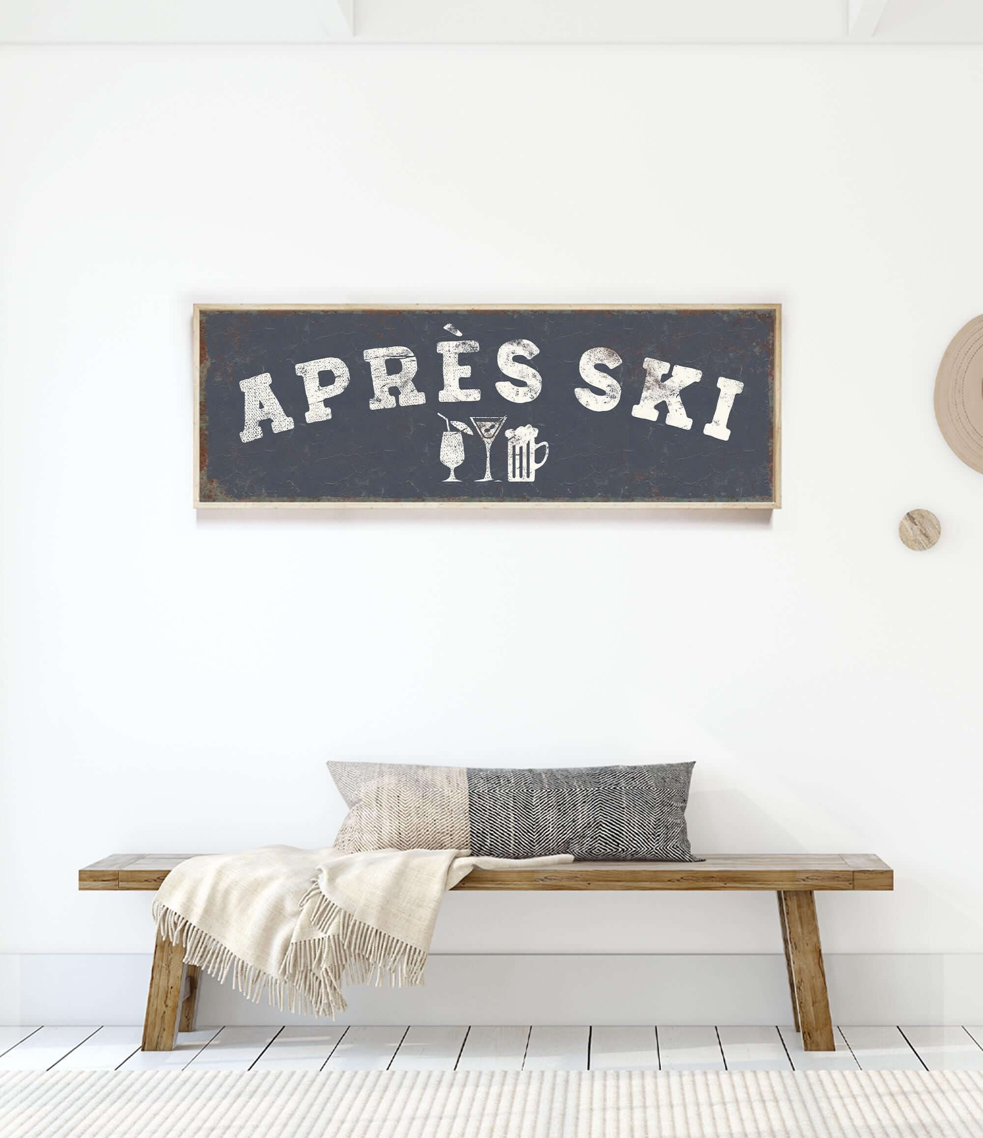 a wooden bench with a gray and white throw blanket on it, and a framed sign above it that says "APRES SKI".