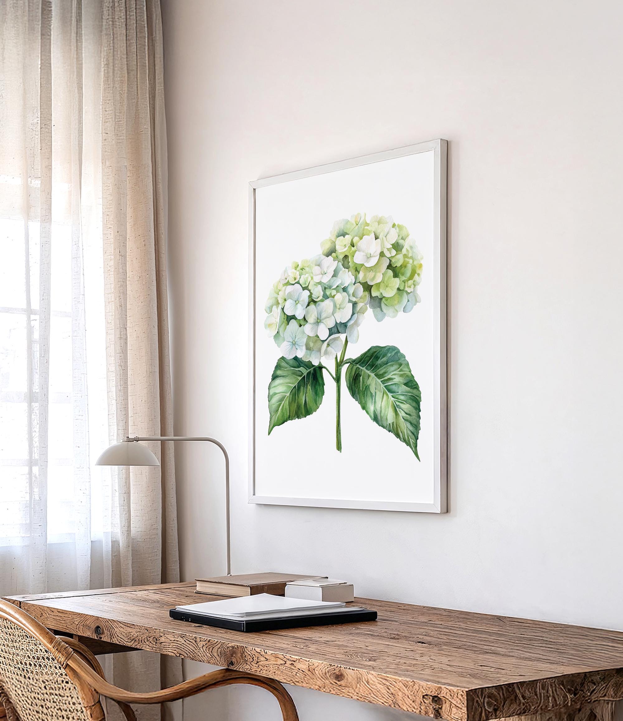 a wooden desk with a lamp, a framed watercolor painting of a green hydrangea flower, and a window with sheer curtains.