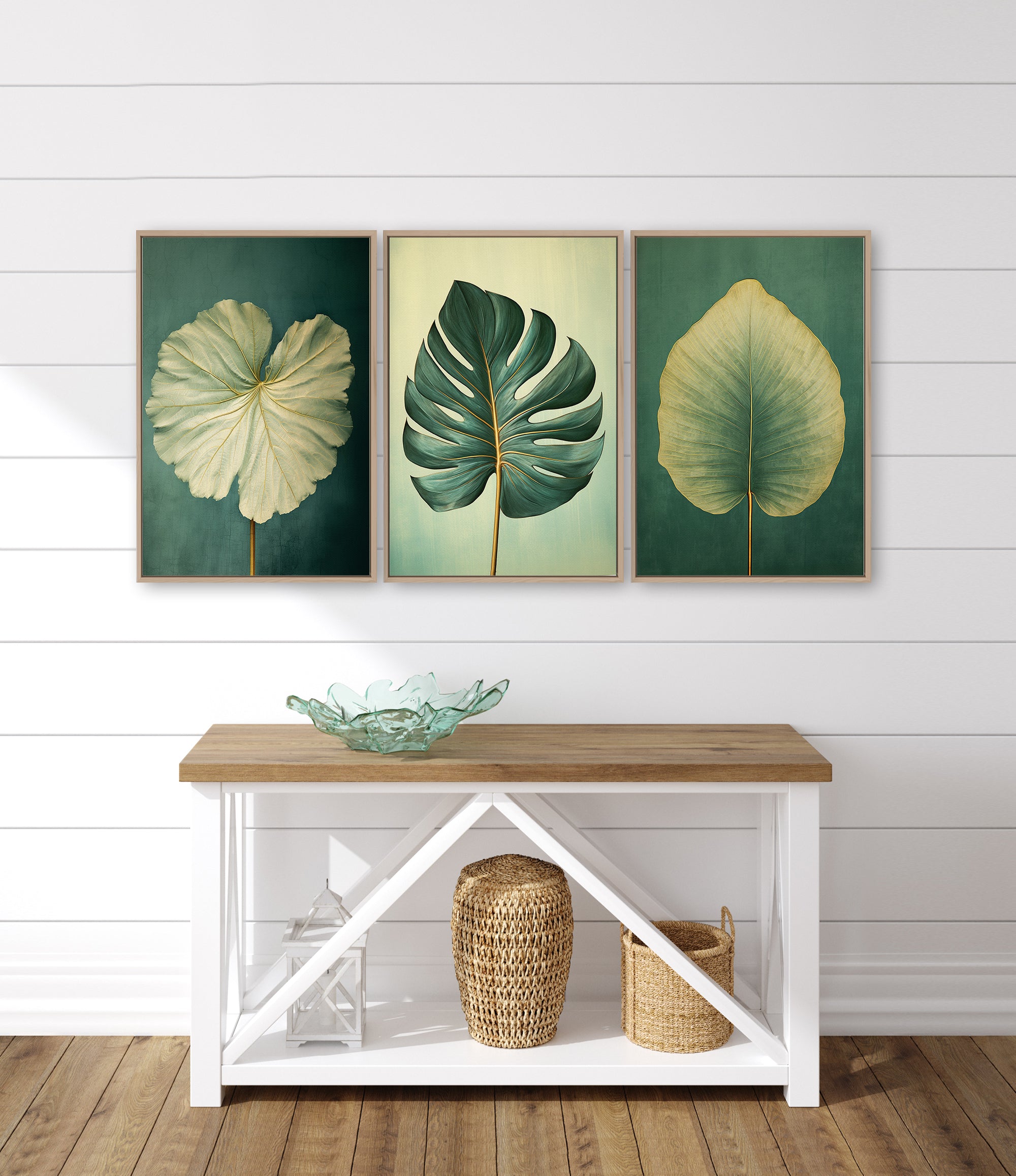 a white console table with three framed leaf artworks displayed above it. The leaves are green and yellow, creating a harmonious color palette. The table also has a glass bowl and a woven basket on it, adding a touch of natural elements to the interior design.