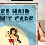 The image is a hand holding a framed print with a vintage-style illustration of a woman with long hair. The text on the print reads "Make hair care" and is in a bold, stylized font.