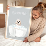 A woman is sitting on a bed holding a framed poster with a dog in a bathtub.