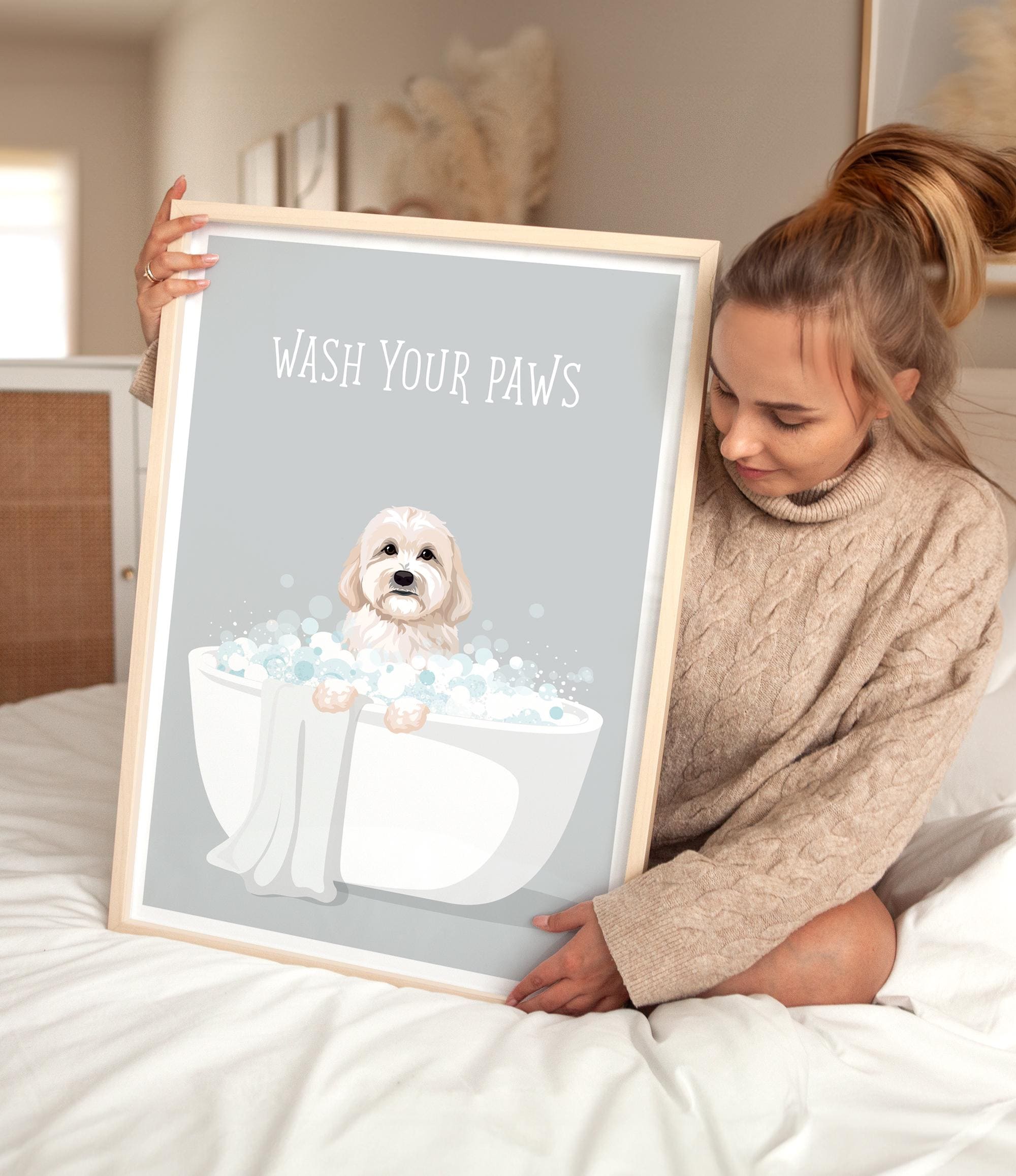 A woman is sitting on a bed holding a framed poster with a dog in a bathtub.