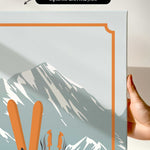 a hand holding a framed print of a mountain landscape with skis and ski poles.