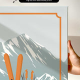 a hand holding a framed print of a mountain landscape with skis and ski poles.