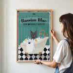 A woman is hanging a framed poster of a cat sitting in a bathtub, which features a Russian Blue cat.