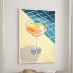 a framed illustration of a cocktail glass filled with orange slices, placed on a wooden table.