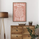 The Beach House Rules Sign, Painted Wood, Coral, adds charm as beach house wall decor when displayed above a wooden dresser next to a lamp and a basket of flowers.