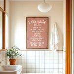 a bathroom with a framed sign that reads "LAKESHOUSE RULES" above a white sink. The sign provides a list of rules for guests to follow while staying at the lake house.