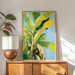 a large, vibrant painting of a banana tree hanging on a wall above a wooden cabinet.