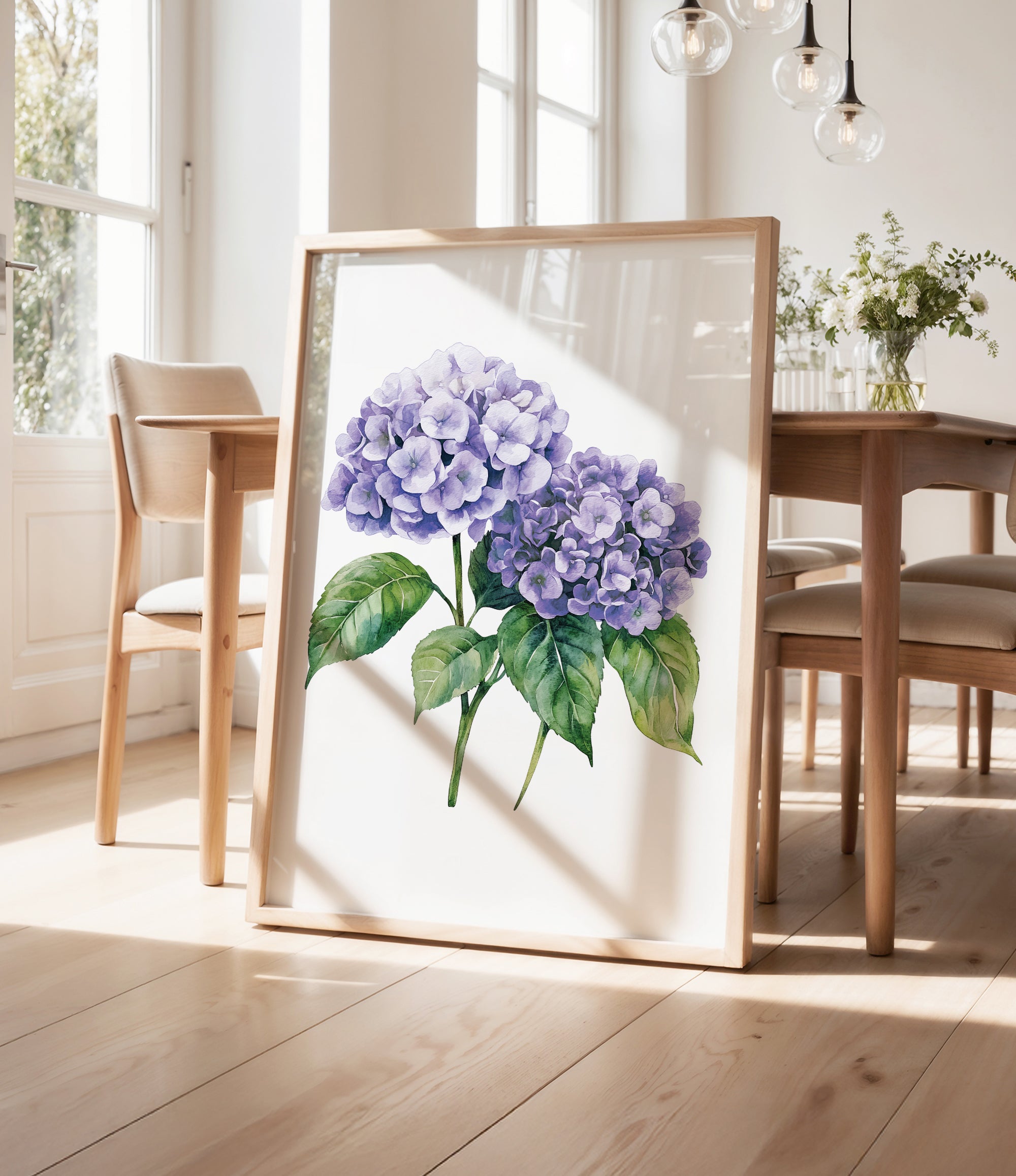 a framed painting of purple hydrangeas on a wooden table, with a vase of greenery and a wooden chair visible in the background.