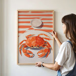 A woman is hanging a framed picture of a crab on a wall.