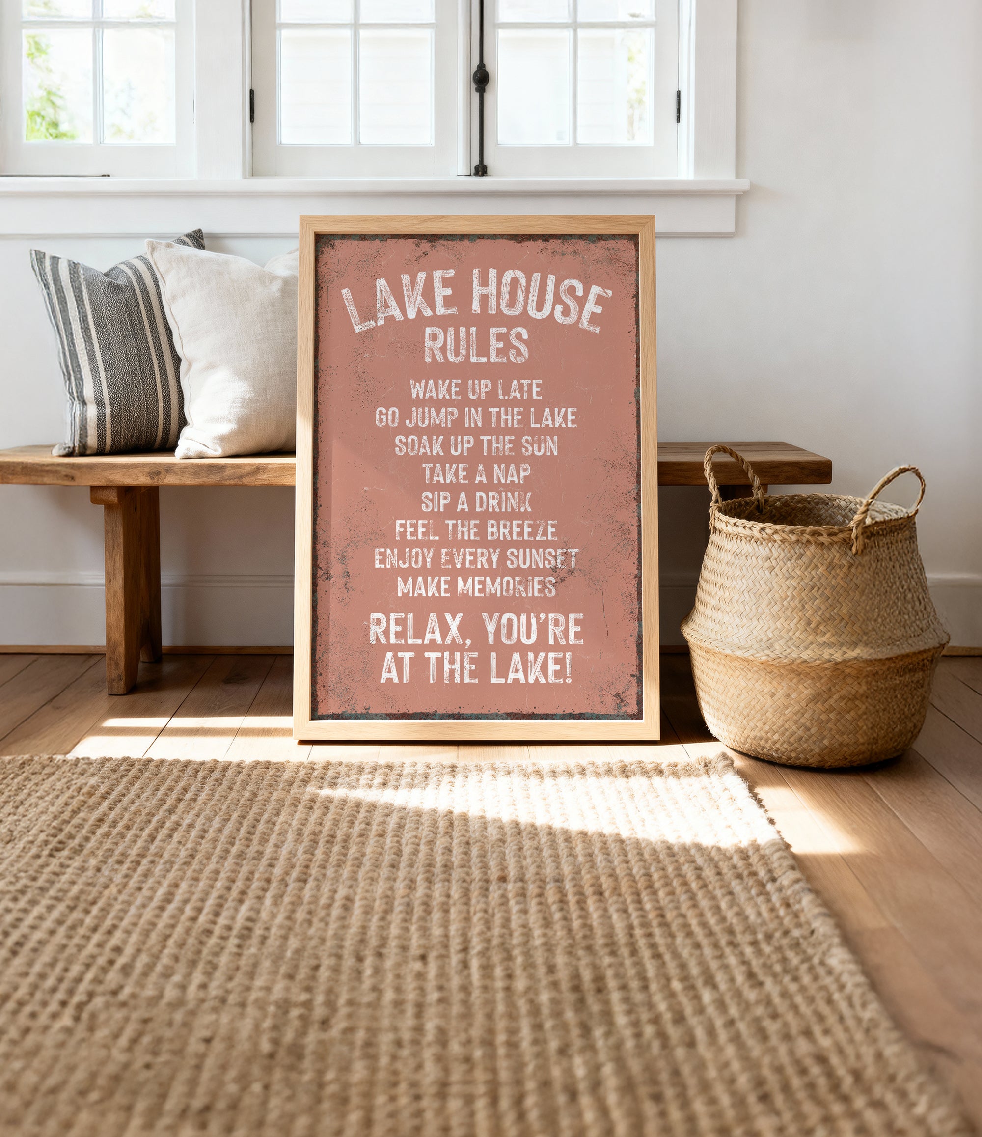 A framed sign with a list of rules for the Lake House, placed on a wooden bench and a woven basket, with a window and a rug in the background.