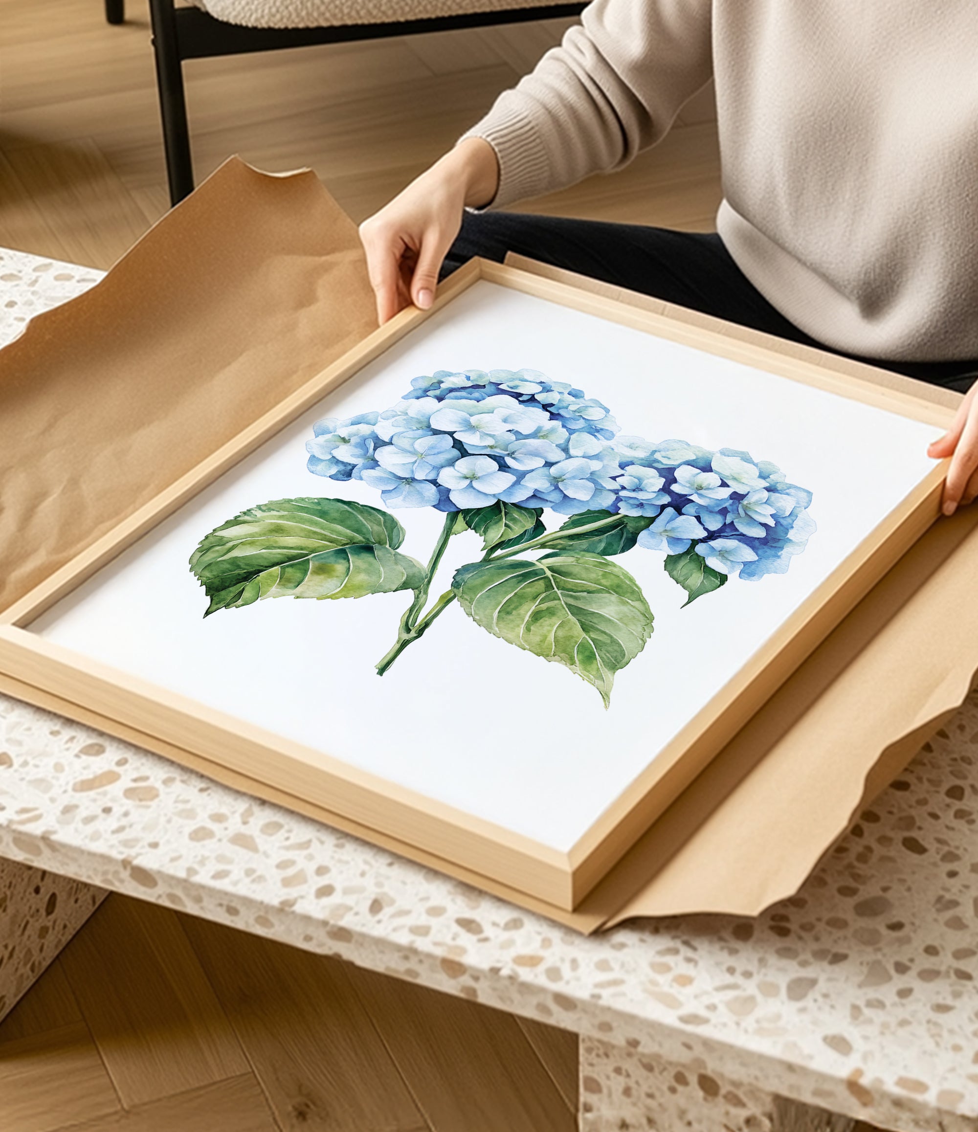 A person is holding a framed painting of blue hydrangea flowers in a wooden frame.