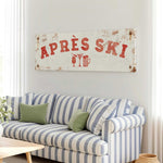 a living room with a striped couch, a coffee table, and a large sign that says "APRES SKI" above the couch.