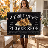 A woman is holding a large sign that reads "Autumn Harvest Flower Shop" with a floral design.