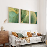 a cozy living room with a white sofa adorned with throw pillows and a blanket. Above the sofa, three framed prints of green leaves are displayed on the wall, creating a harmonious and visually appealing space.