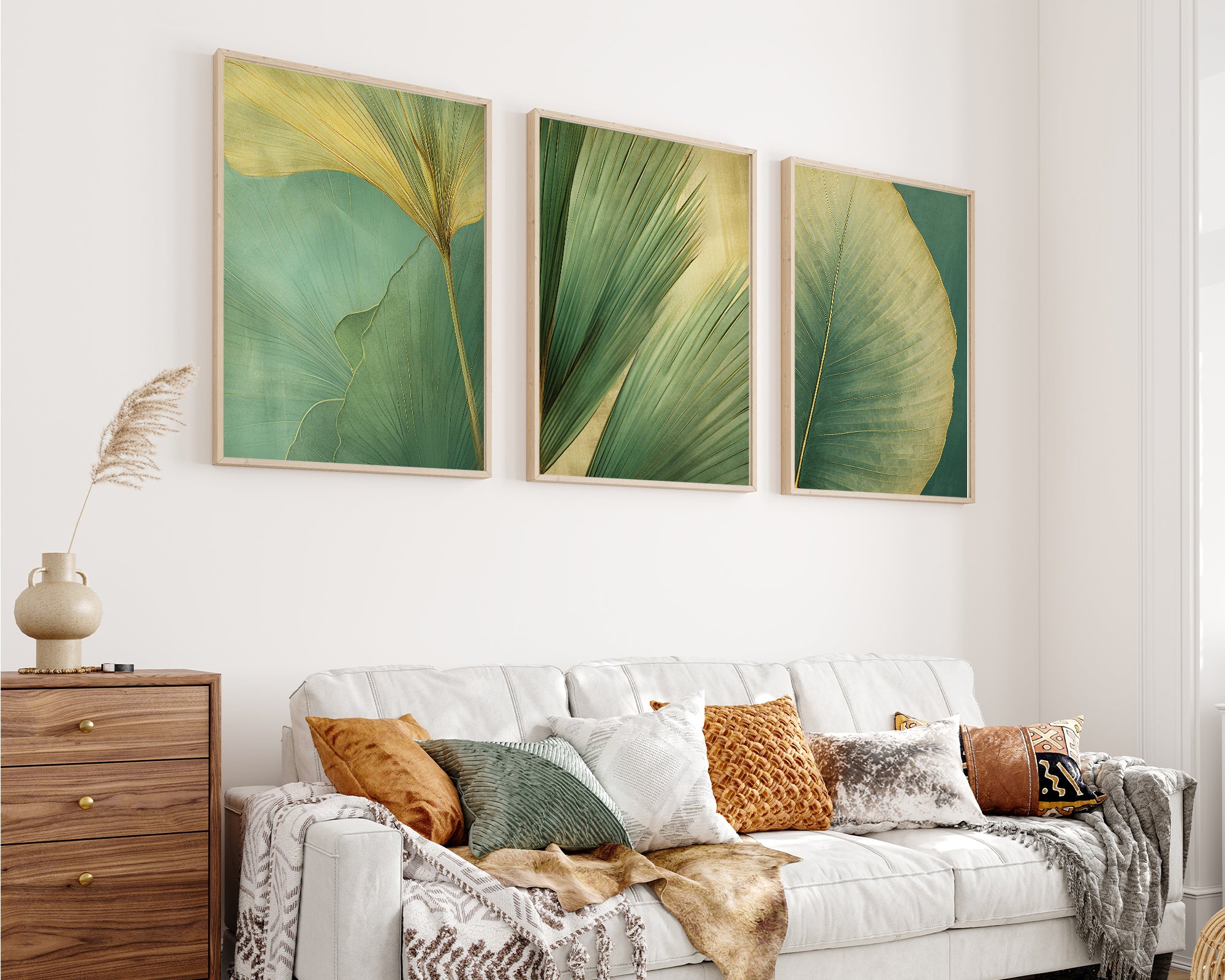 a cozy living room with a white sofa adorned with throw pillows and a blanket. Above the sofa, three framed prints of green leaves are displayed on the wall, creating a harmonious and visually appealing space.
