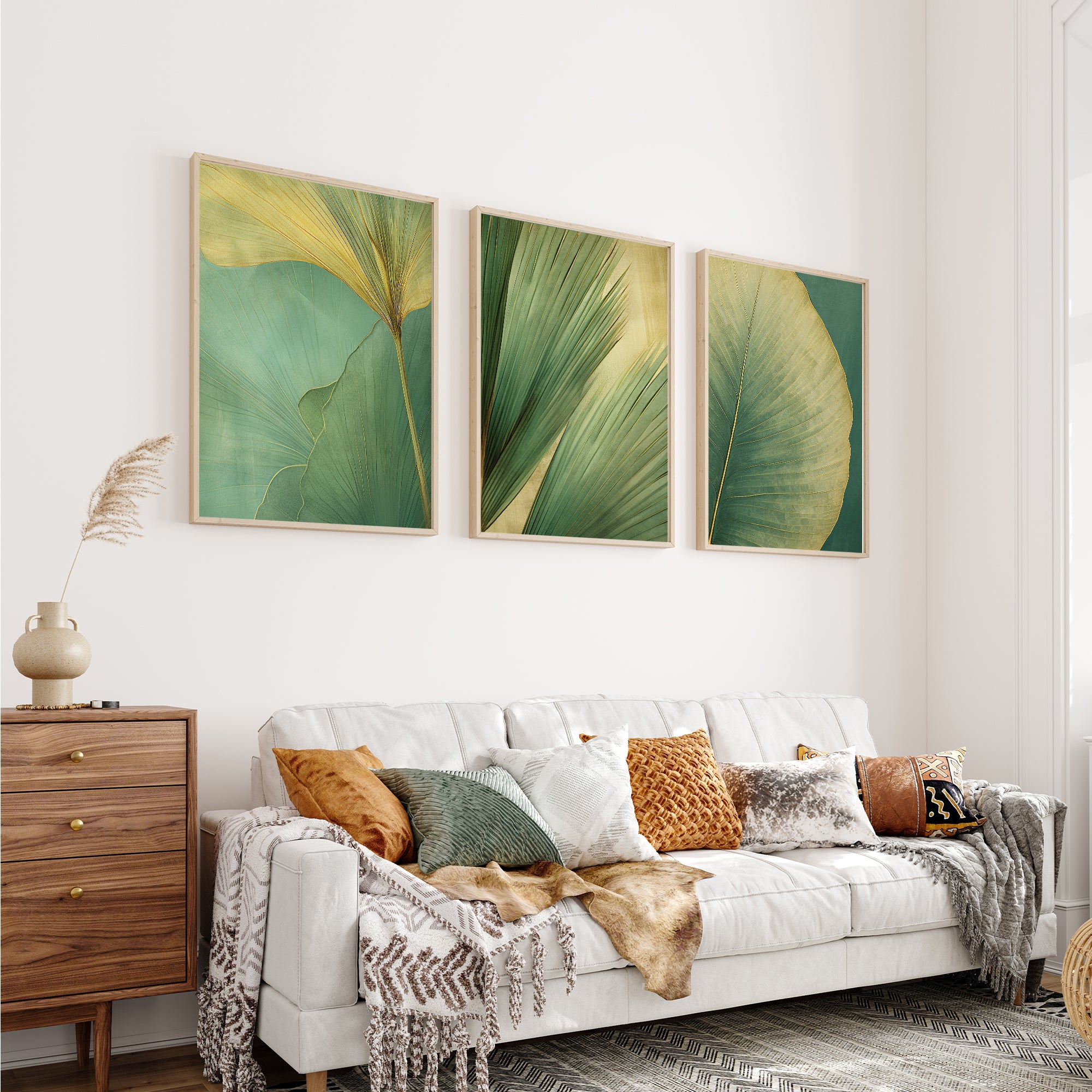 a cozy living room with a white sofa adorned with throw pillows and a blanket. Above the sofa, three framed prints of green leaves are displayed on the wall, creating a harmonious and visually appealing space.