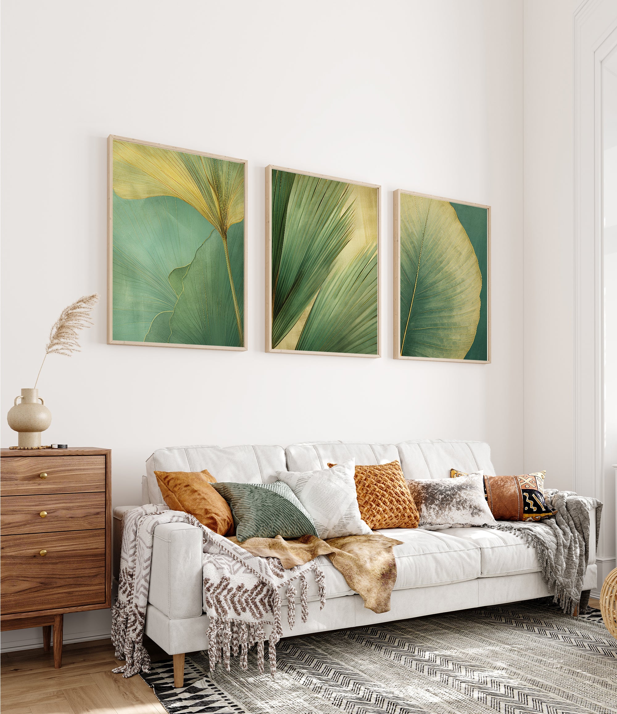 a cozy living room with a white sofa adorned with throw pillows and a blanket. Above the sofa, three framed prints of green leaves are displayed on the wall, creating a harmonious and visually appealing space.