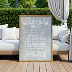 a wooden sign with a beach-themed message, placed on a wooden deck with a white couch and a white curtain in the background.