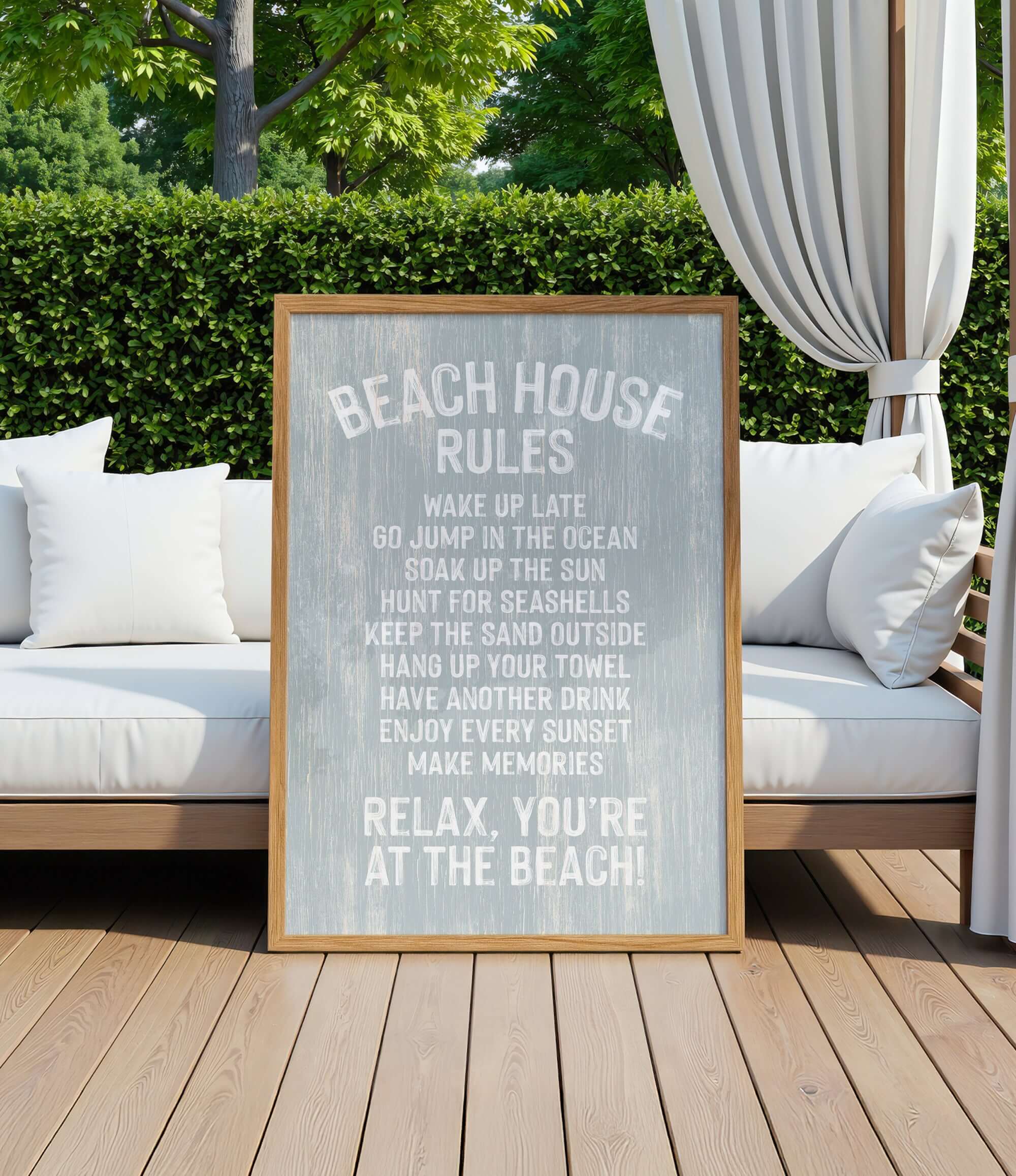 a wooden sign with a beach-themed message, placed on a wooden deck with a white couch and a white curtain in the background.