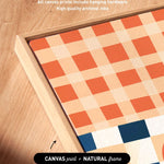 a close-up view of a wooden surface with a canvas print and a natural frame. The canvas print has a checkered pattern in shades of orange and white, and the natural frame complements the print. The text above the image states that artwork wraps around the sides of the canvas, and all canvas prints include hanging hardware. The text below the image indicates that the print is a "CANVAS print + NATURAL frame".