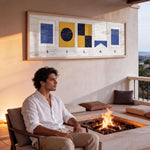 A man sits on a chair in front of a fireplace, with a framed artwork hanging on the wall behind him.