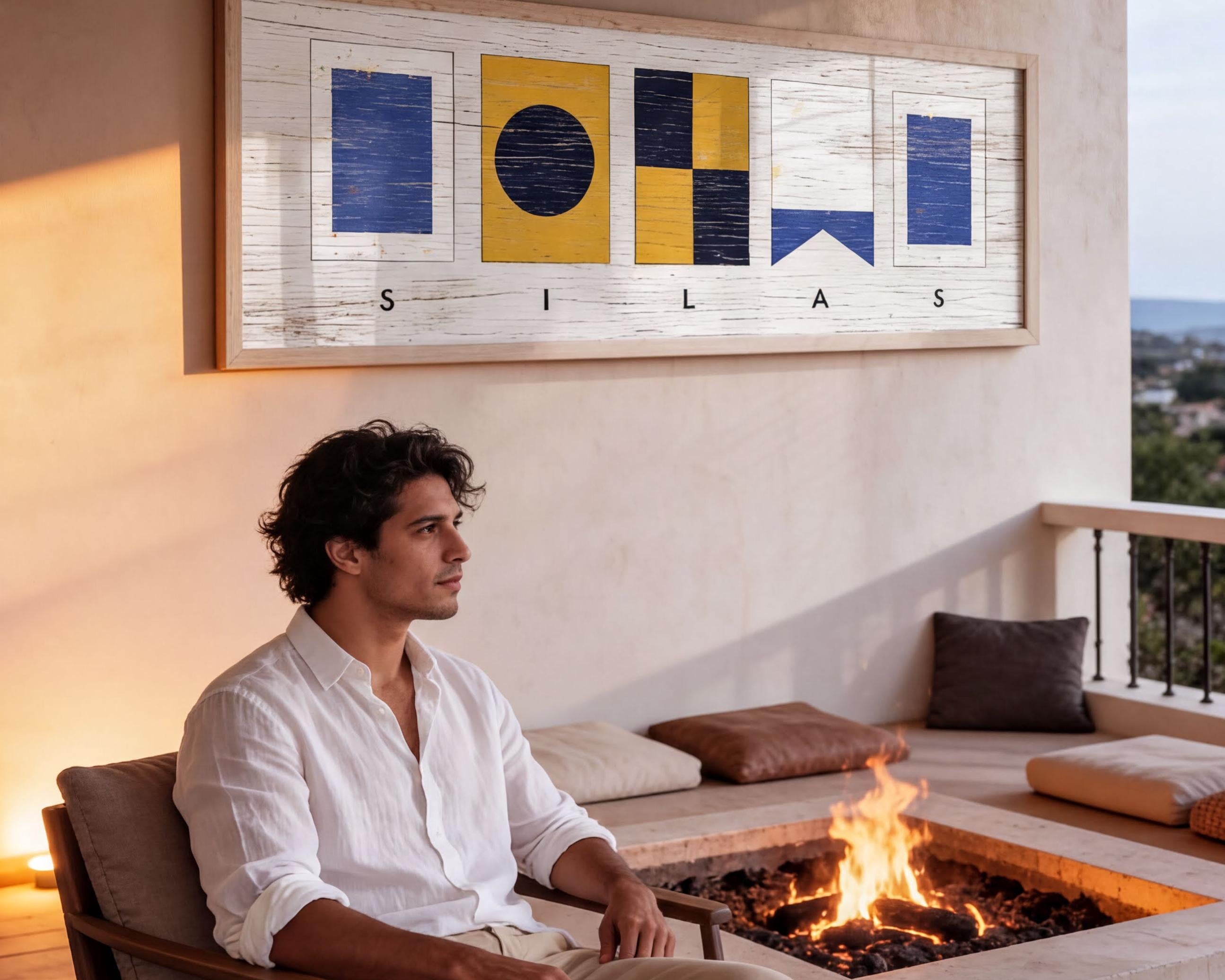 A man sits on a chair in front of a fireplace, with a framed artwork hanging on the wall behind him.