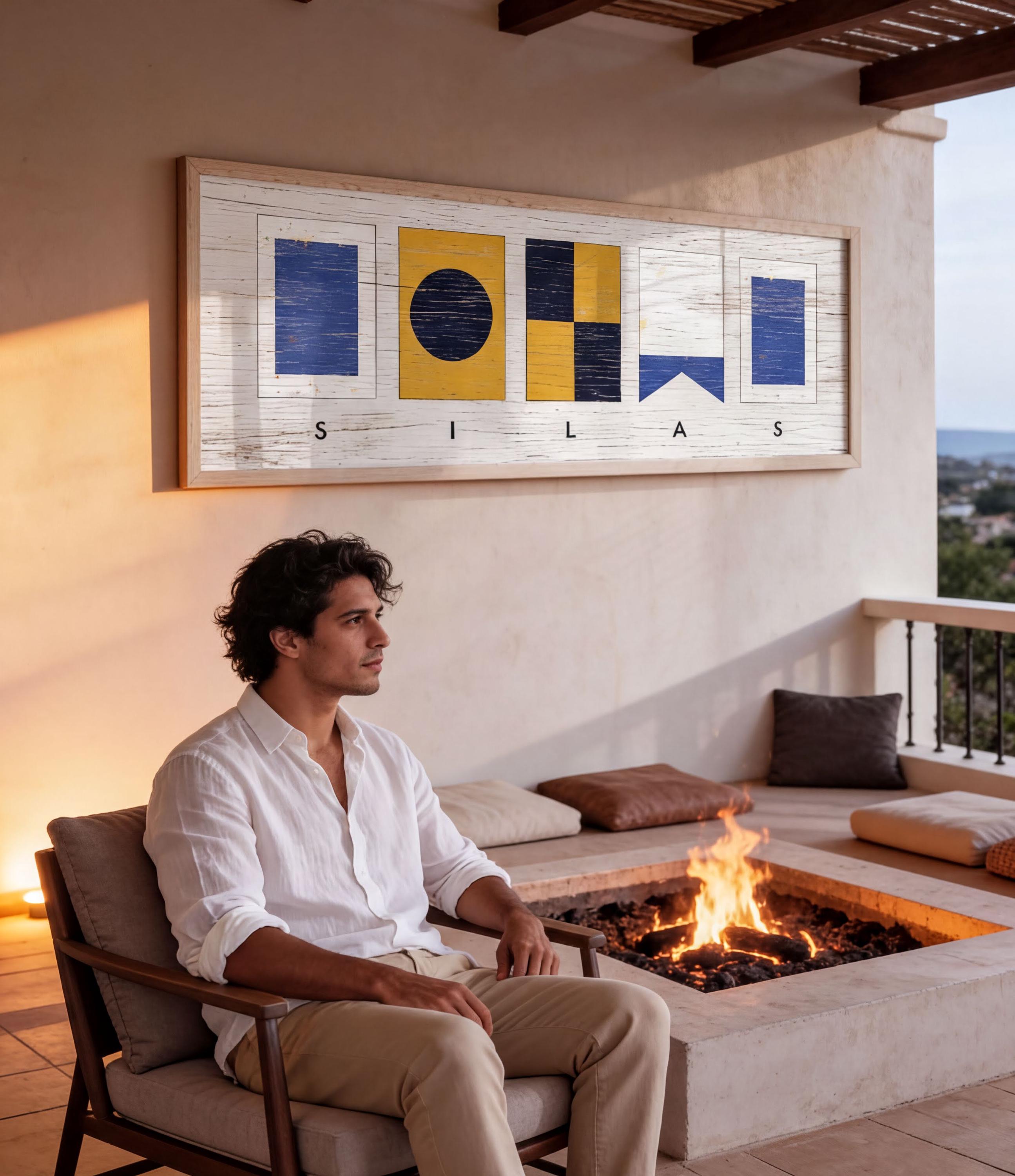 A man sits on a chair in front of a fireplace, with a framed artwork hanging on the wall behind him.