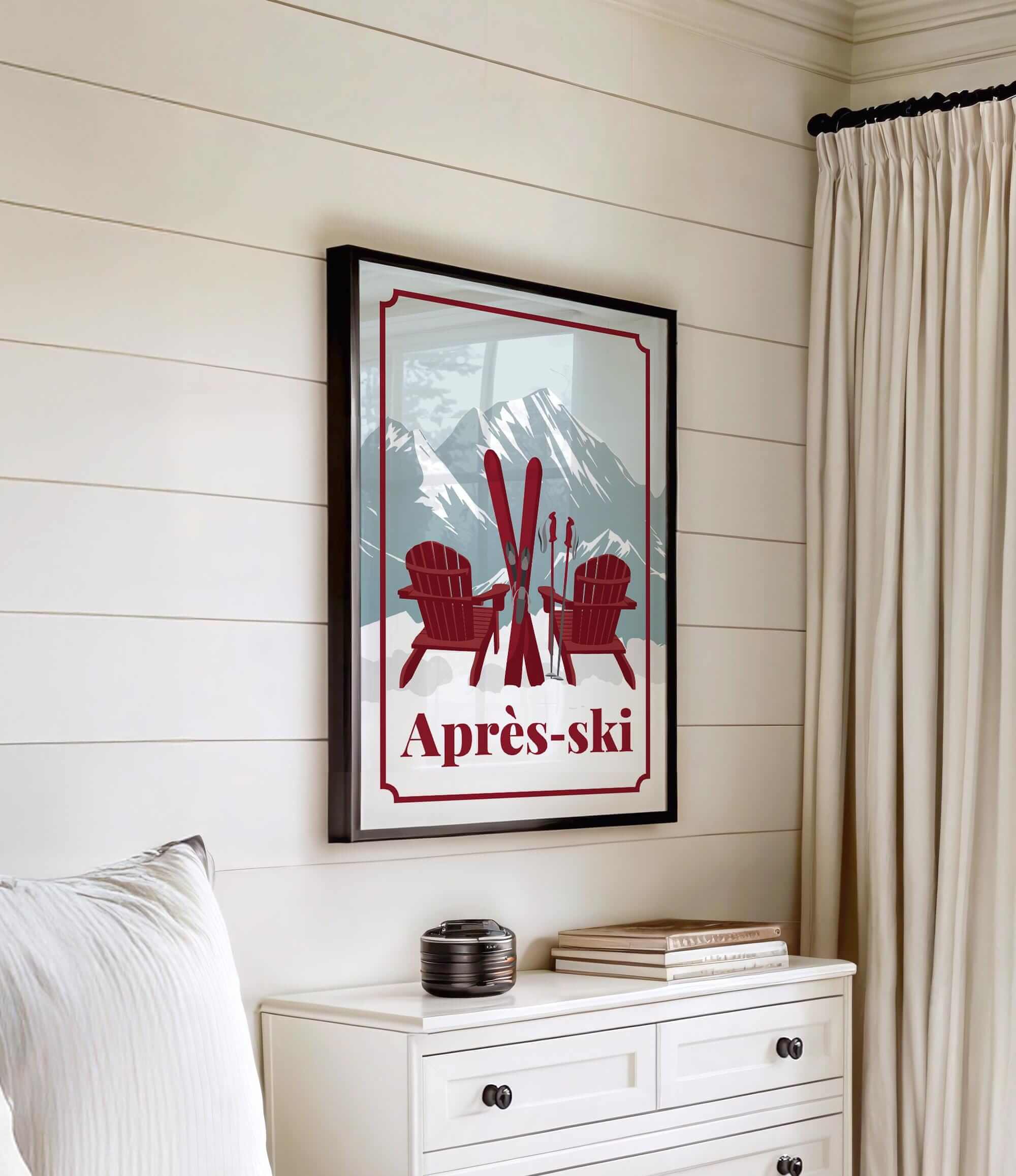 a framed poster of a mountain landscape with two red Adirondack chairs and skis, hanging on a wall above a white dresser.