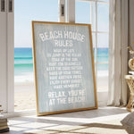 a framed sign with beach-themed rules, placed in a room with a view of the ocean through a window.
