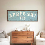 a wooden dresser with a framed sign above it that says "APRÈS SKI", and there are two white chairs and a vase with flowers on the dresser.