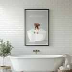 A framed poster with a cartoon image of a dog sitting in a bathtub, accompanied by the text "WASH YOUR PAWS" is displayed on a white tiled wall above a white clawfoot bathtub.