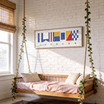 a cozy bedroom with a wooden bed suspended from the ceiling by ropes, creating a unique and comfortable sleeping space. The bed is adorned with white pillows and a pink blanket, adding a touch of warmth and comfort to the room. Above the bed, there is a framed artwork depicting nautical flags, adding a nautical theme to the space. The room is also decorated with potted plants, which contribute to the overall pleasant and inviting atmosphere.