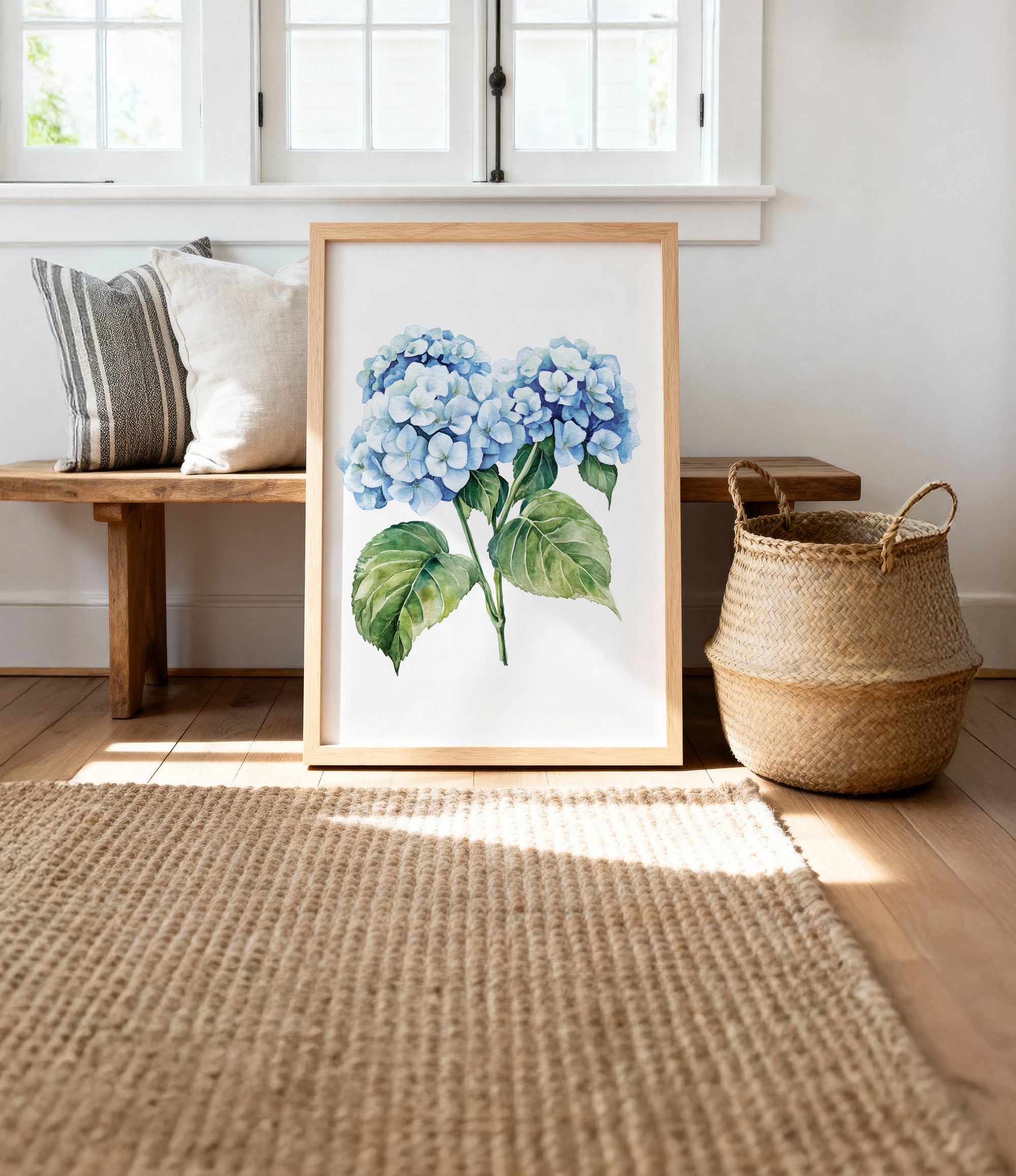 a framed painting of blue hydrangea flowers on a wooden bench, with a woven basket and a woven rug on the floor in the background.
