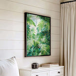 a white dresser with a framed painting of lush green palm leaves hanging on the wall above it.