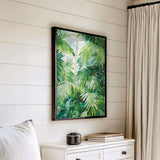 a white dresser with a framed painting of lush green palm leaves hanging on the wall above it.