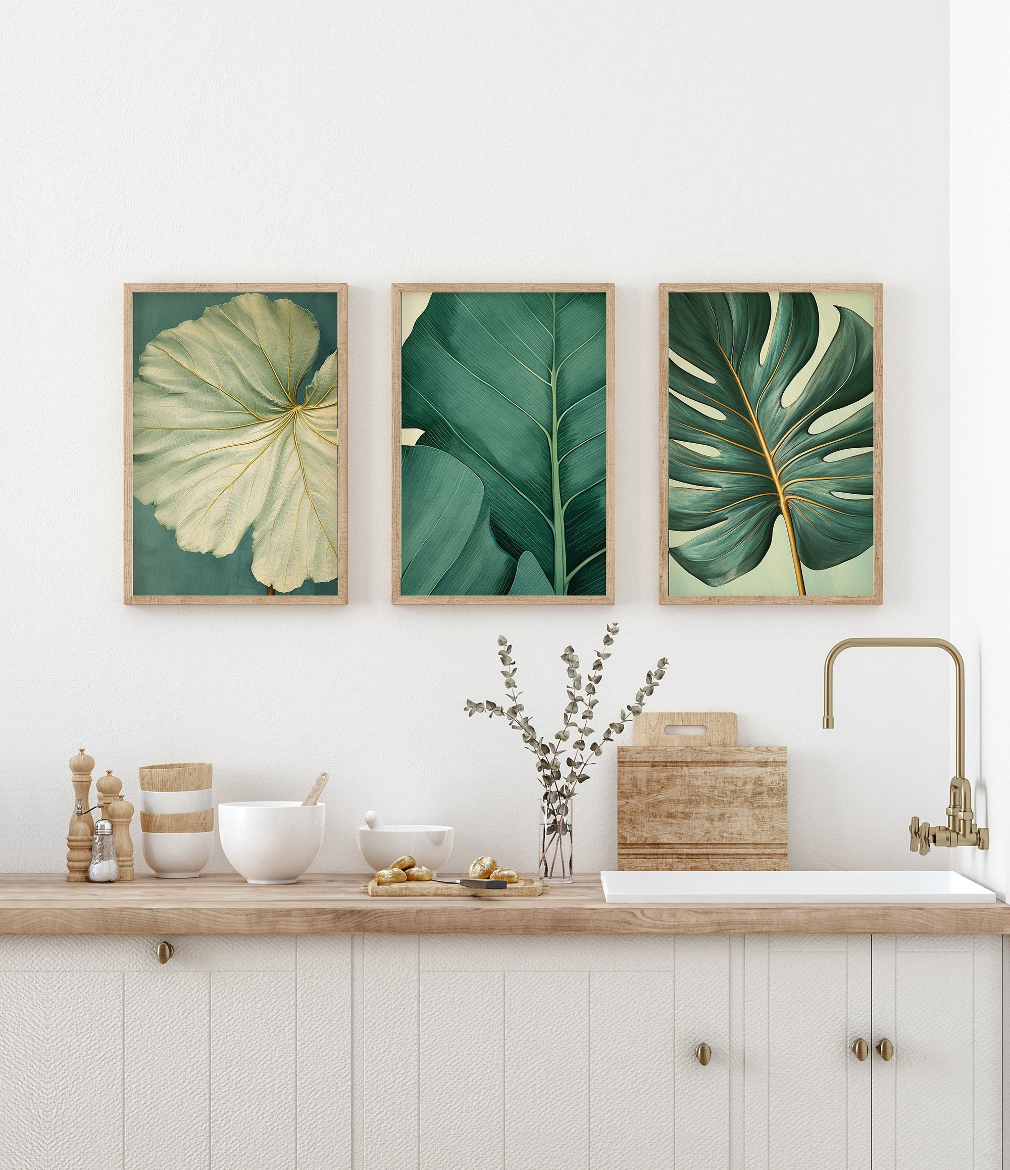 a kitchen counter with three framed botanical leaf prints displayed above it. The prints showcase various shades of green leaves, adding a touch of nature to the space. The kitchen counter also has a sink, bowls, and other kitchen accessories, creating a functional and organized appearance.
