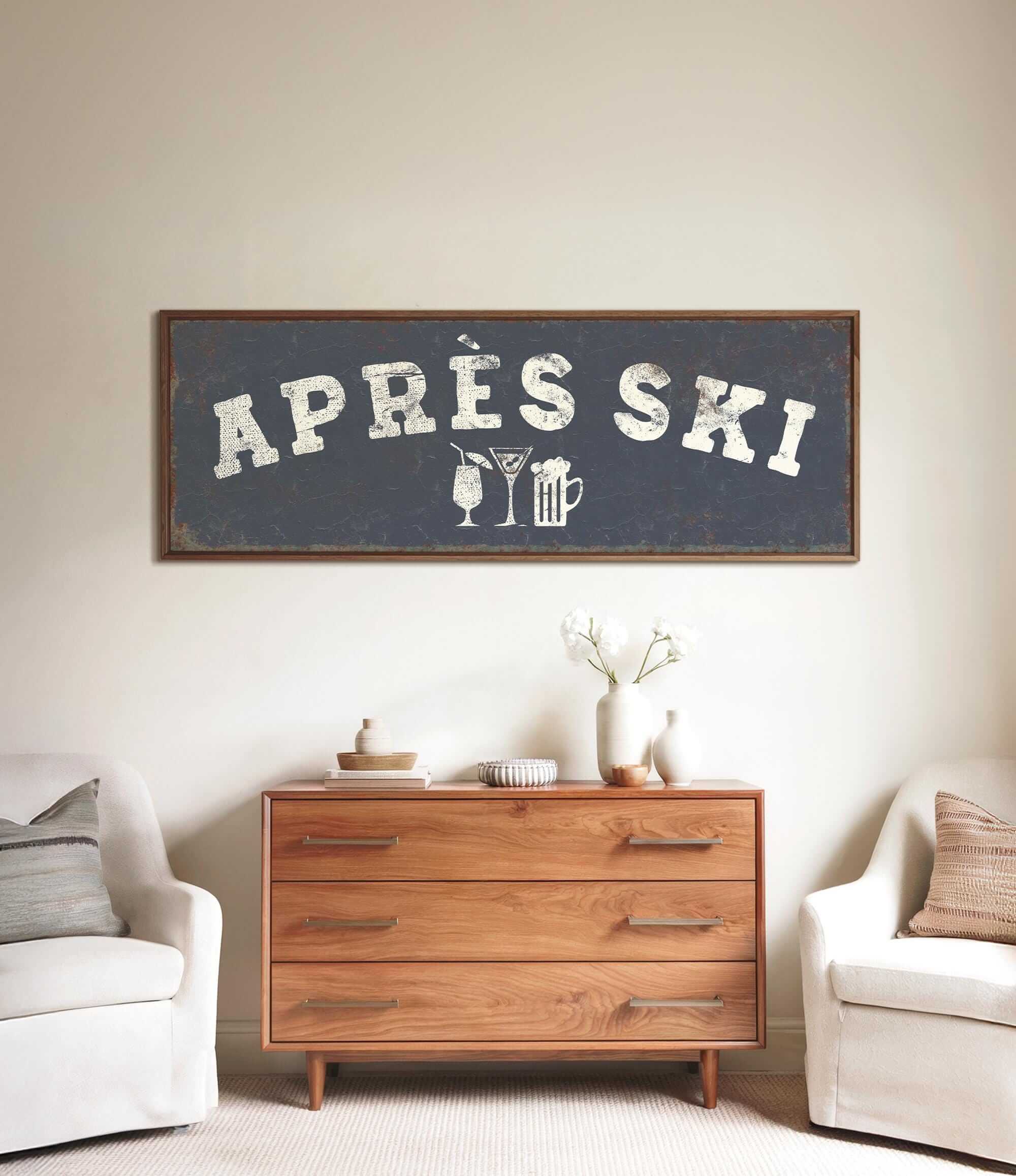 a wooden dresser with a framed sign above it that says "APRÈS SKI", and there are two white chairs and a vase with flowers placed in front of the dresser.