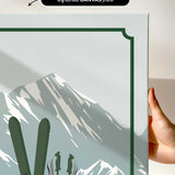 a hand holding a framed print of a mountain landscape with skis and ski poles.