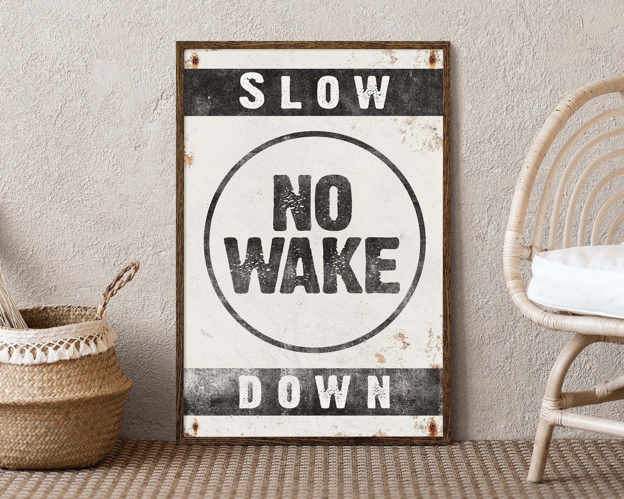 A No Wake Sign, Black on White, leans against a textured wall by a wicker chair—ideal lake house wall decor that adds modern farmhouse charm.