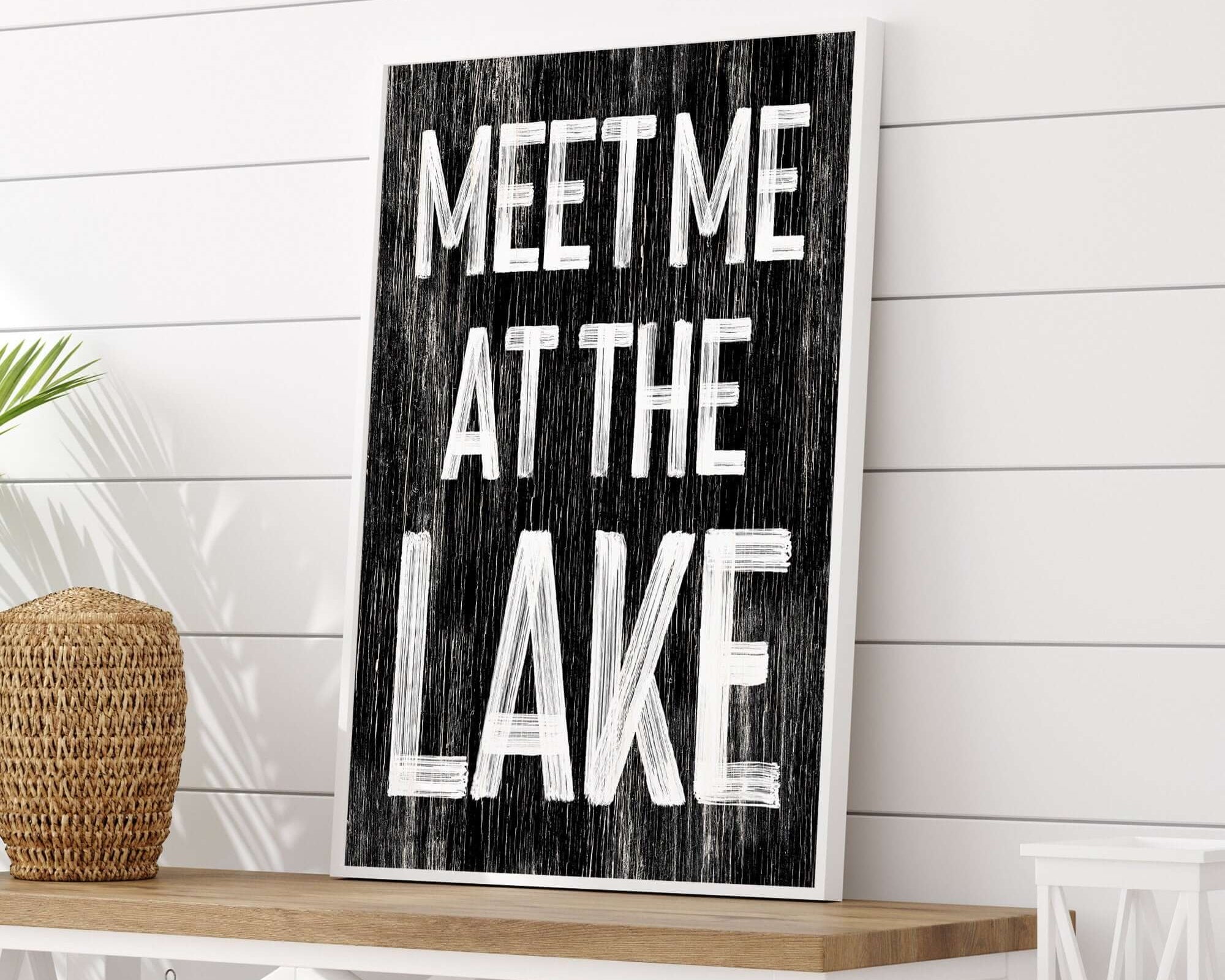 The Meet Me at the Lake Sign, Black features bold white letters on a framed vintage design—ideal decor for any lake house.