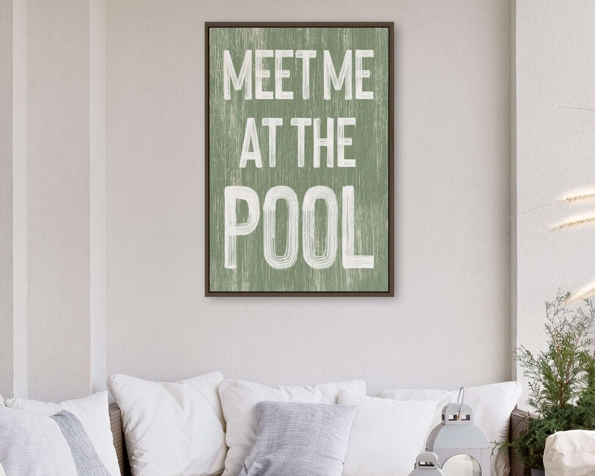 A Meet Me at the Pool Sign in seagrass hangs above a white outdoor sofa with cushions, adding the perfect summer home vibe.