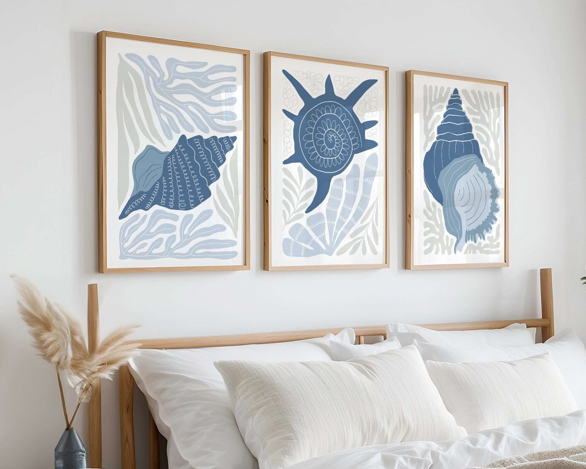 The Ocean Blocks Triptych | Set of Three Prints | 344 hangs above a neatly made bed with white bedding, bringing a touch of coastal wall art and serene blue seashell imagery to this cozy, minimalist bedroom.