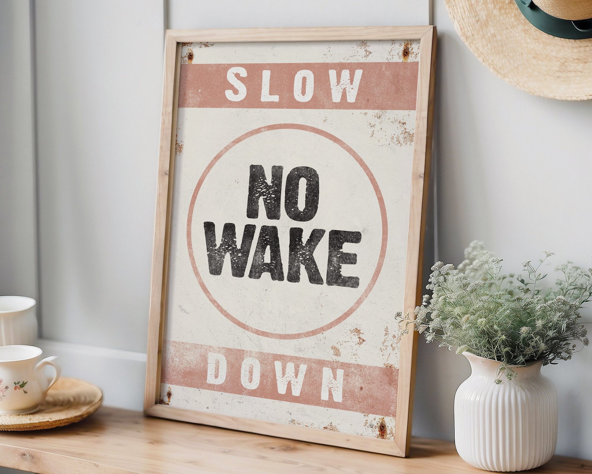 The No Wake Sign, Coral on White, is a framed vintage piece reading "Slow Down, No Wake"—ideal lake house wall decor for your table or shelf alongside plants and summer accessories.