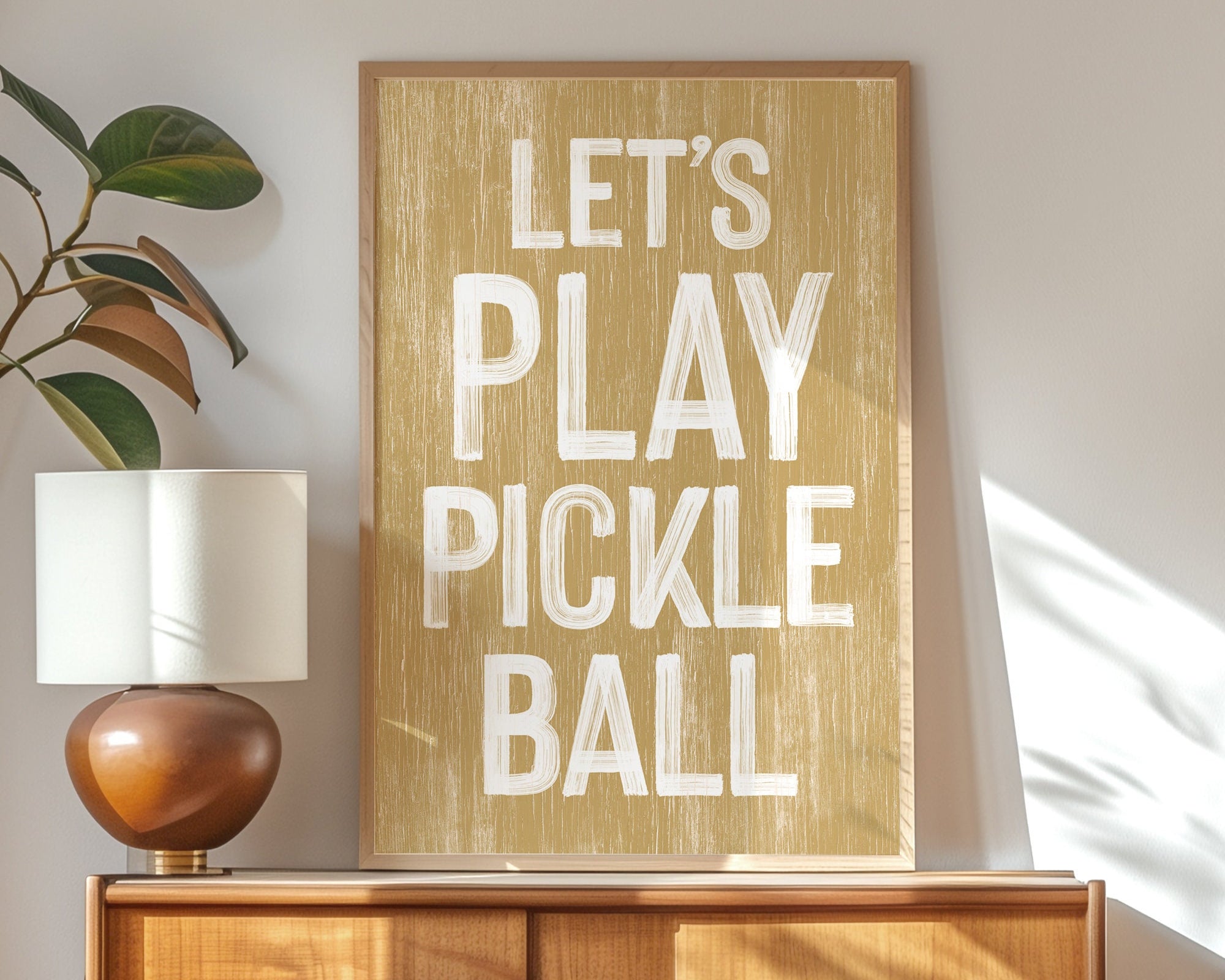 The Let’s Play Pickleball Sign, Butternut, features bold white text—ideal wall decor for modern farmhouse spaces and perfect for any pickleball enthusiast’s display.