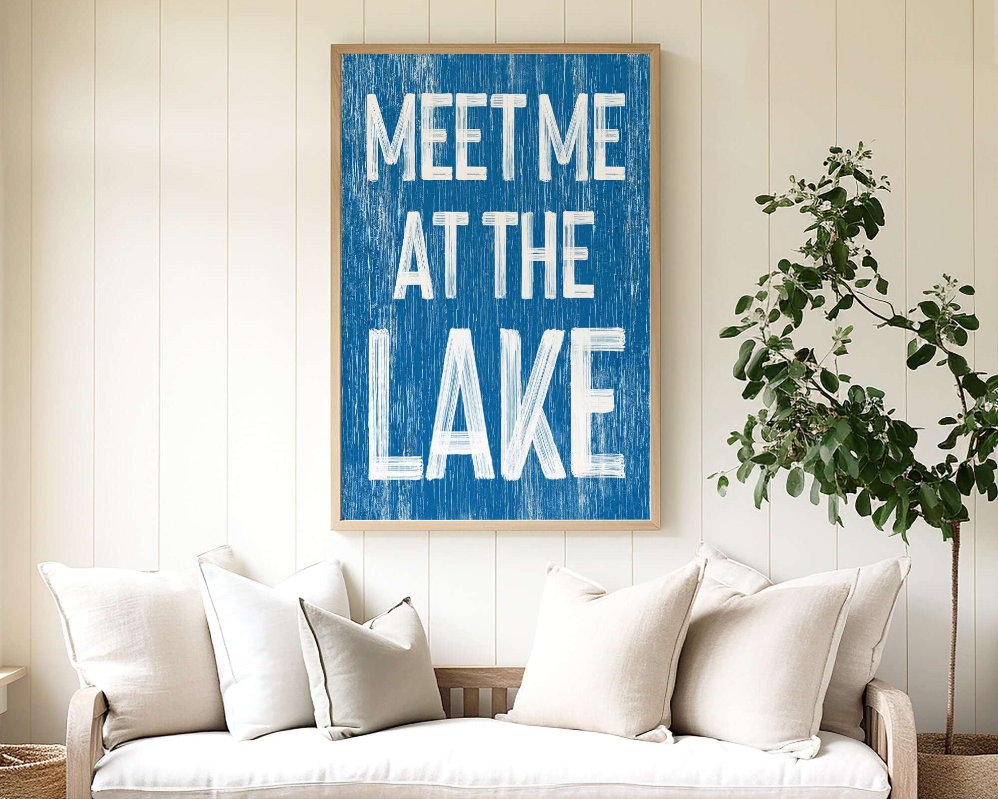 A cozy sofa with white pillows sits beneath the Meet Me at the Lake Sign in Ocean Blue, adding perfect lake house decor charm.