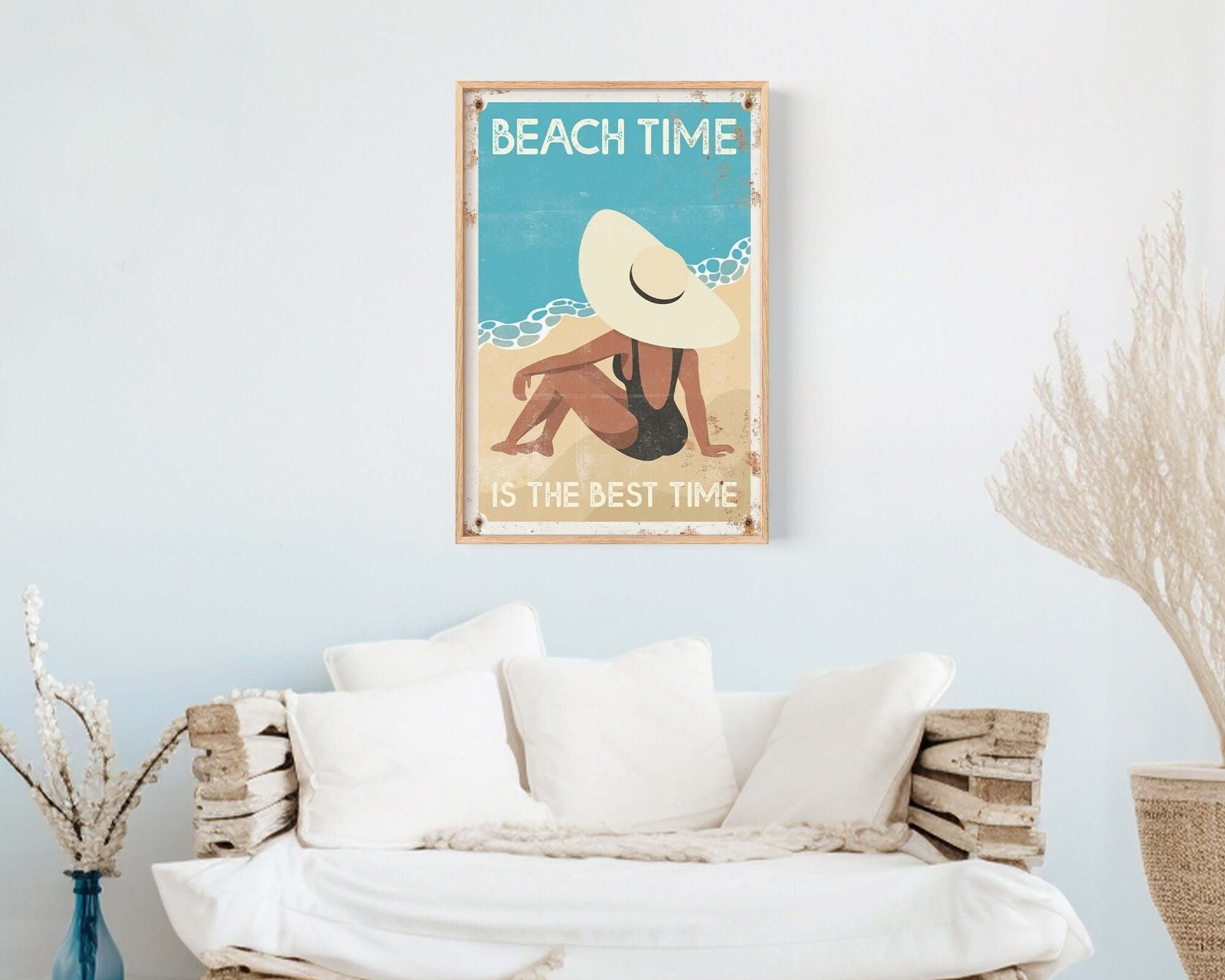 Cozy white couch with pillows sits beneath the "Beach Time is the Best Time, Retro Beach Poster" in a bright, minimalist room.