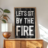 a black and white sign that says let's sit by the fire